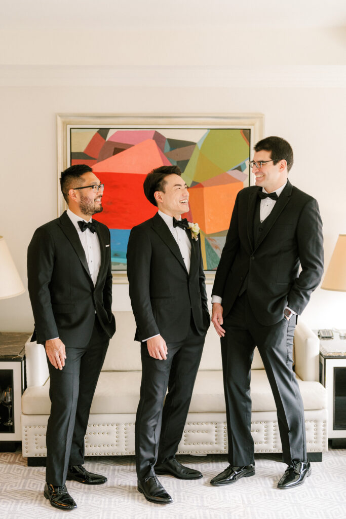 Groom and groomsmen in tuxes laughing in front of a painting at Lotte palace hotel 
