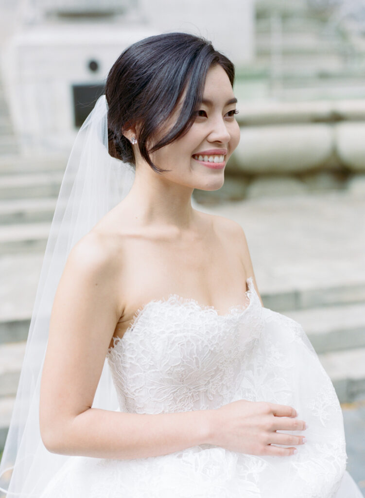 Smiling Korean bride with natural makeup and loose low updo hair with strapless lace wedding dress and veil 