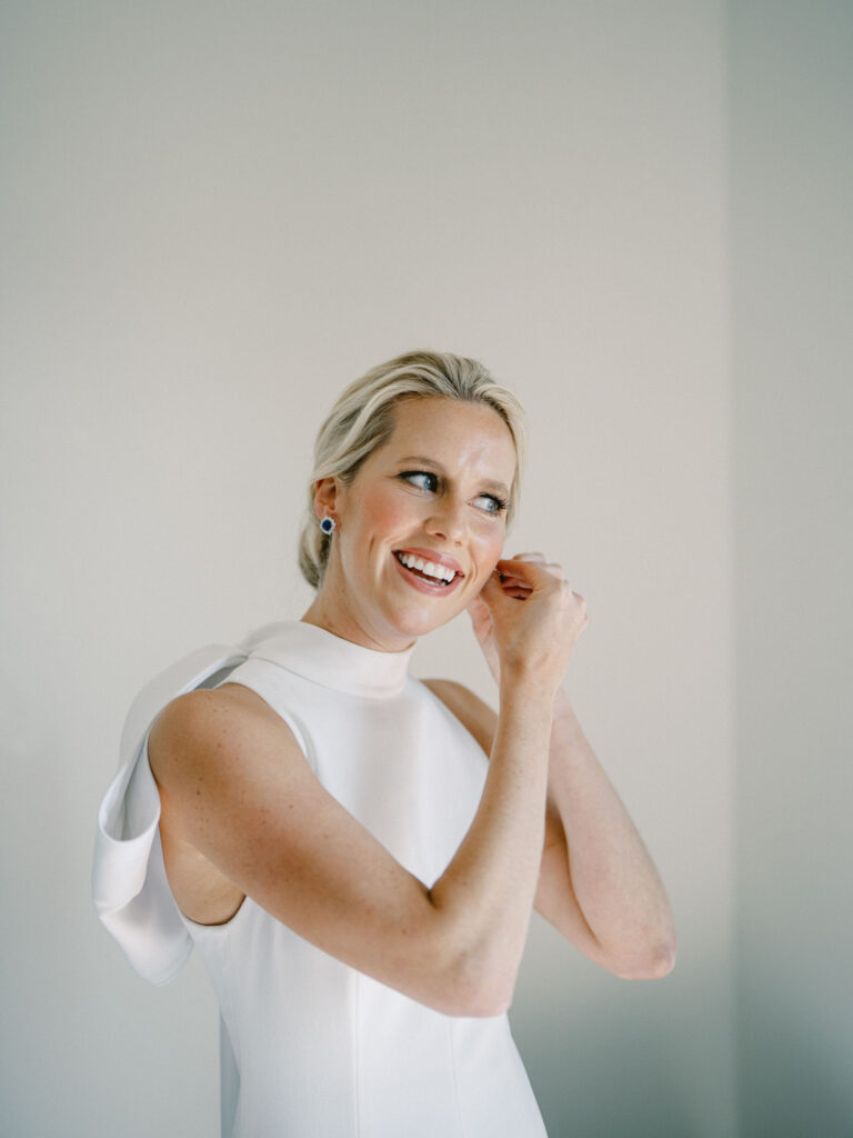 bride putting on earrings and smiling in high neck wedding dress 