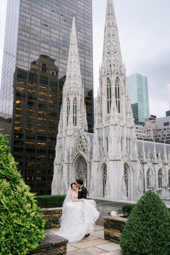 Groom kissing bride in front of St. Patrick's Cathedral in NYC on rooftop of 620 Loft & Garden 