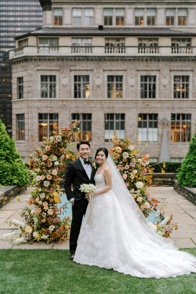 Bride and groom standing in front of fall floral arch wedding day lace ballgown Monique Lhuillier at 620 Loft & Garden in New York City 