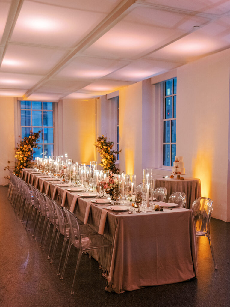 Indoor wedding with long table at 620 Loft & Garden inside the loft space with warm uplighting and taper candles on table designed by East Made Co 