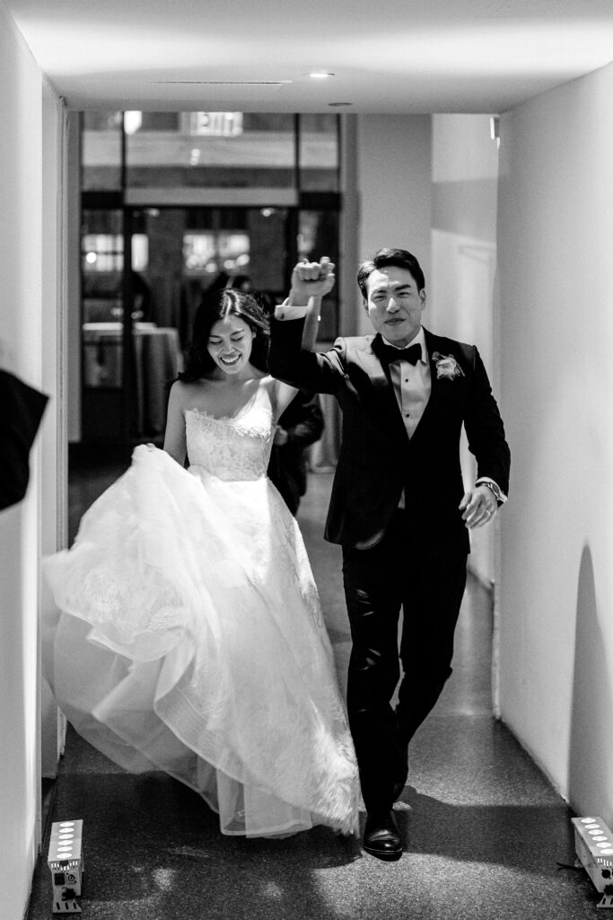 Bride and groom entering their wedding reception in black and white smiling 