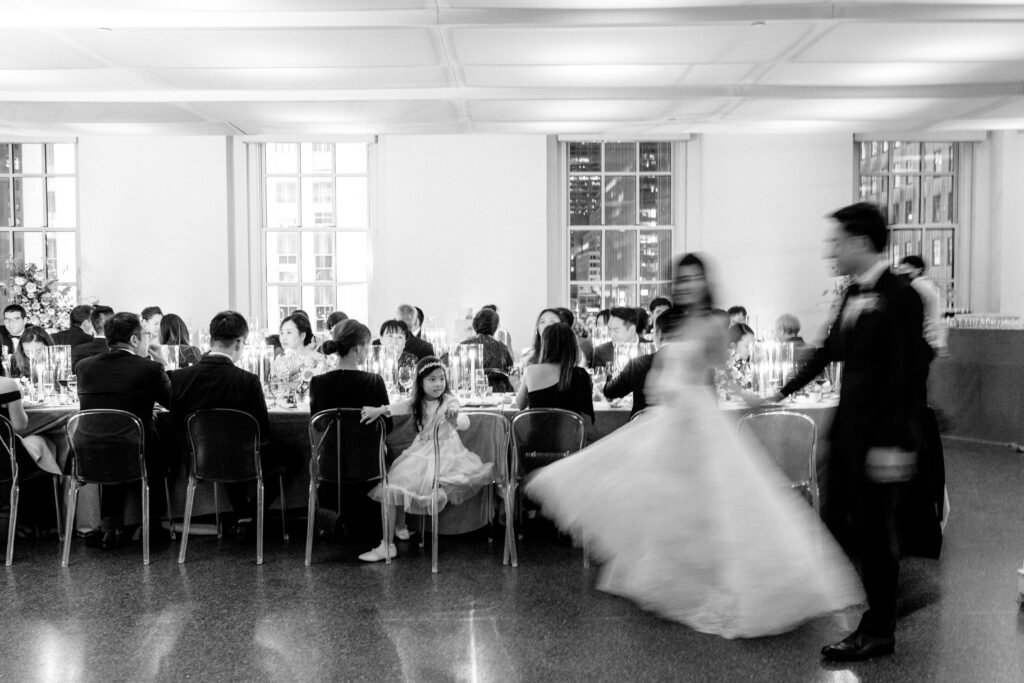 Bride and groom in black and white walking through their wedding reception in blurry motion photo 