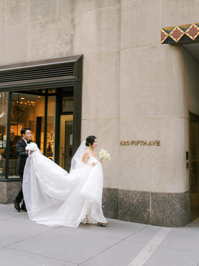 Groom holding bride's dress walking into 620 Fifth Ave wedding venue