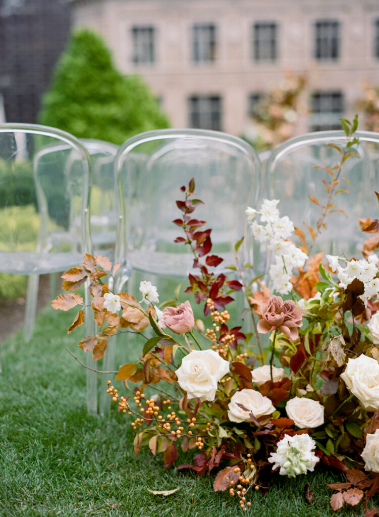 Fall foliage floral detail behind ghost chairs for outdoor NYC wedding ceremony 