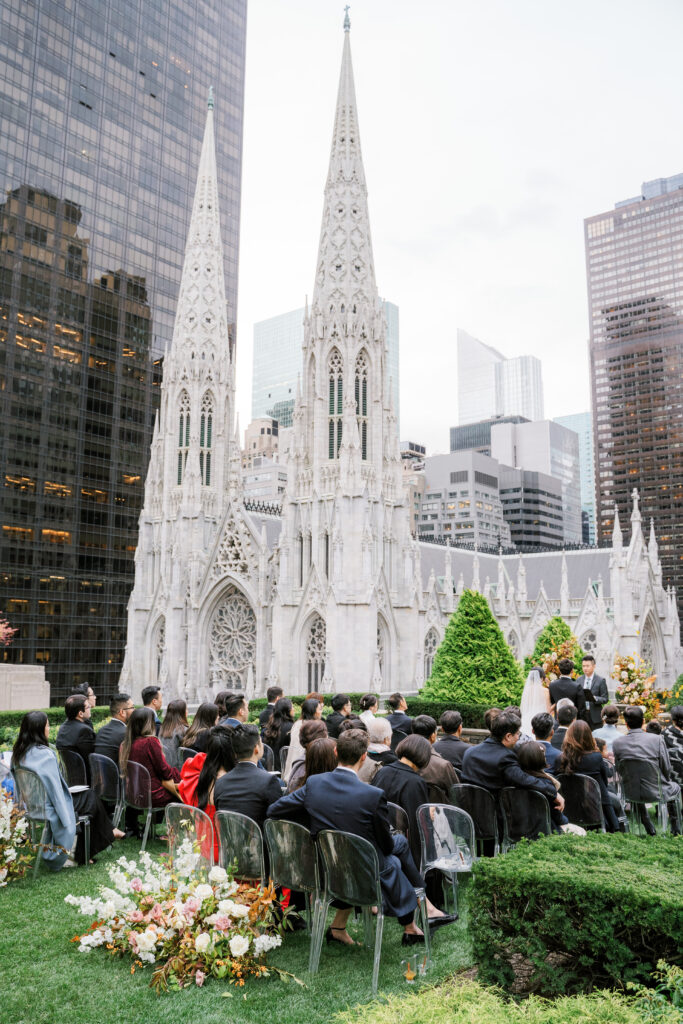 Full wedding ceremony view at 620 Loft & Garden overlooking St. Patrick's Cathedral with wedding guests in ghost chairs 