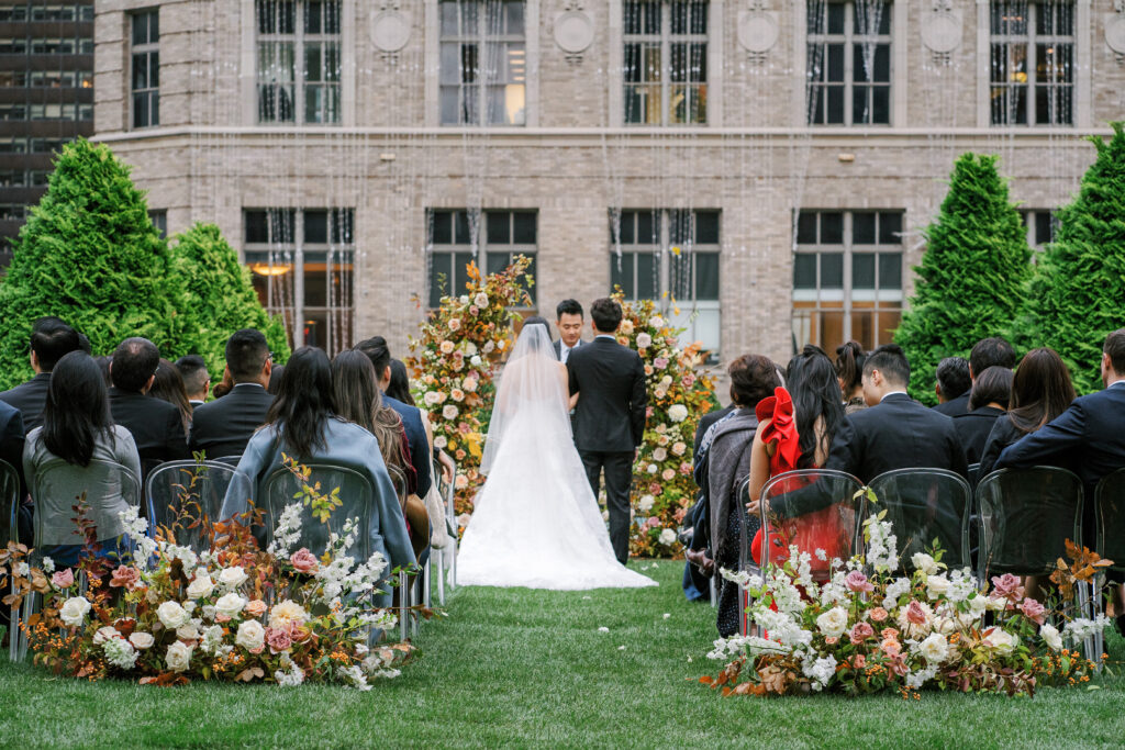 Bride and groom at outdoor rooftop wedding in NYC standing in front of autumn floral arch and Saks Fifth Ave