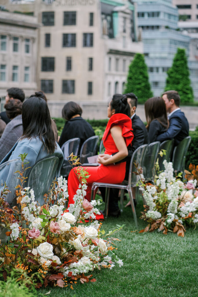 Wedding guest in red dress with puff sleeve detail watching ceremony with autumn florals on ground 