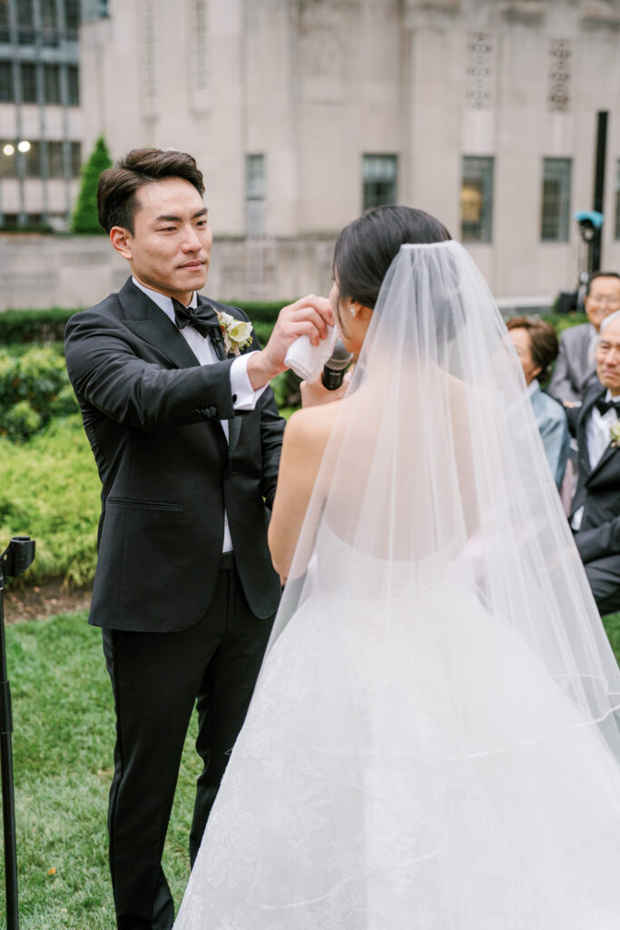 Groom wiping tear from bride's cheek at their rooftop wedding ceremony 