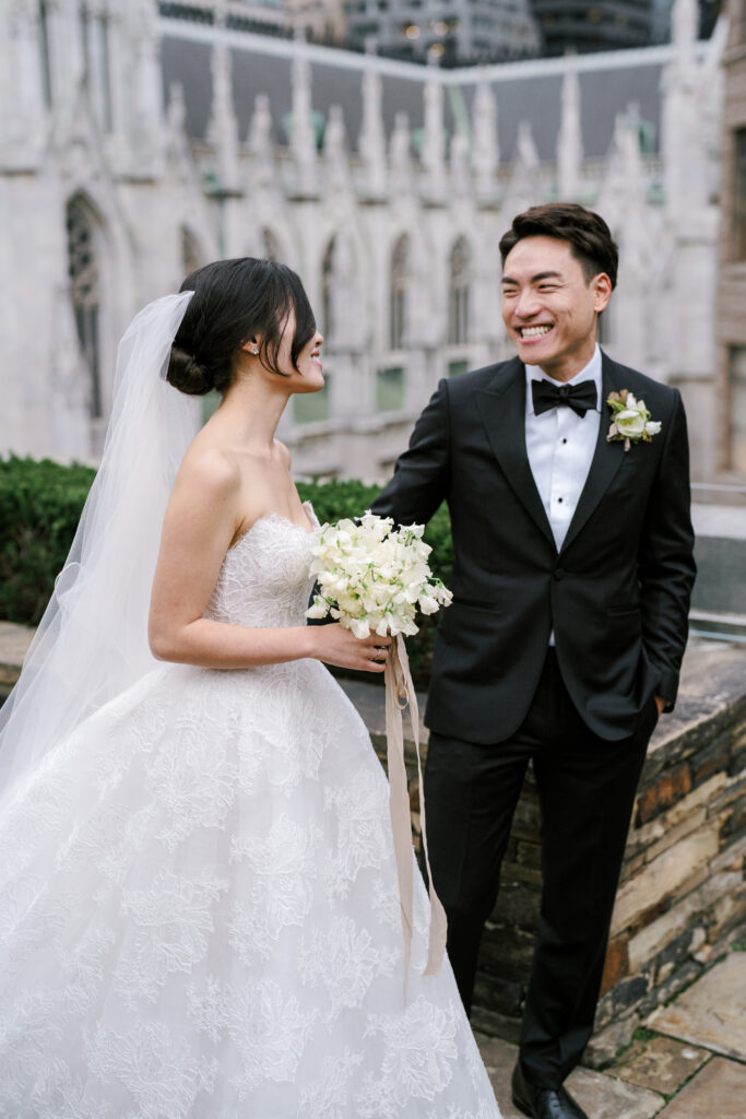 bride and groom laughing on wedding day wearing a black tux and a white lace ballgown 