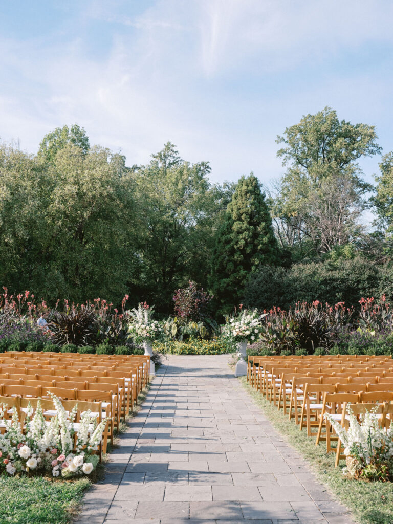 outdoor wedding ceremony with wooden folding chairs and florals on ground at cylburn arboretum in baltimore 