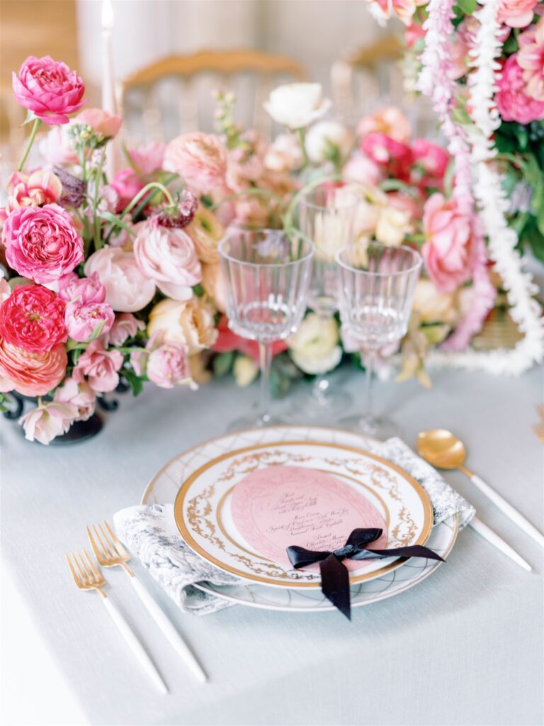 Wedding table place setting with modern gold and white flatware and oval pink menu with black bow