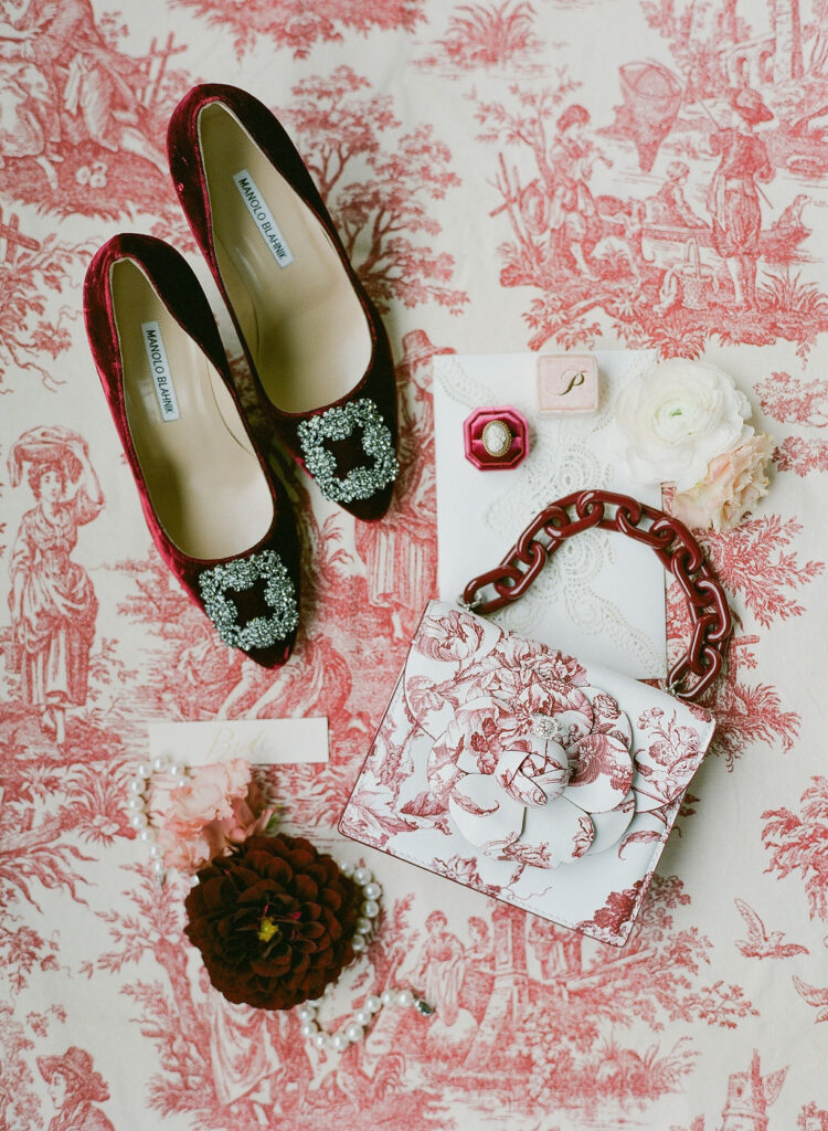 bridal details flatlay with burgundy velvet manolo blahnik heels and dior toile purse bag styled by east made co 