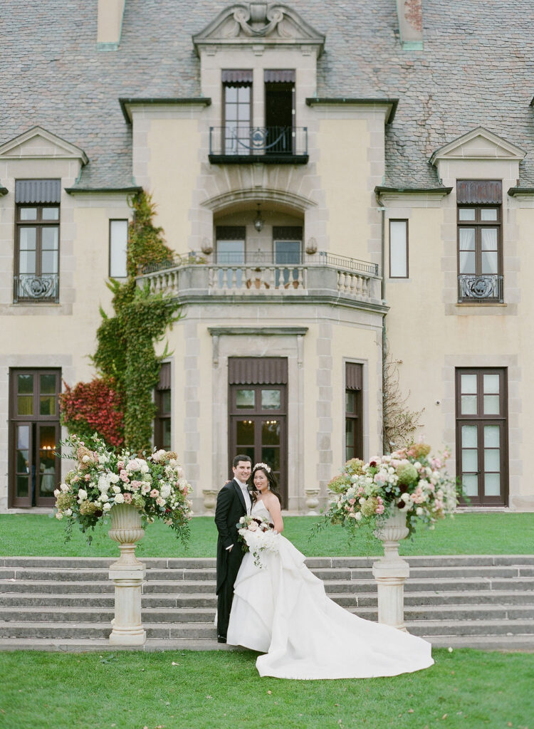 bride and groom in front of oheka castle with floral urns 