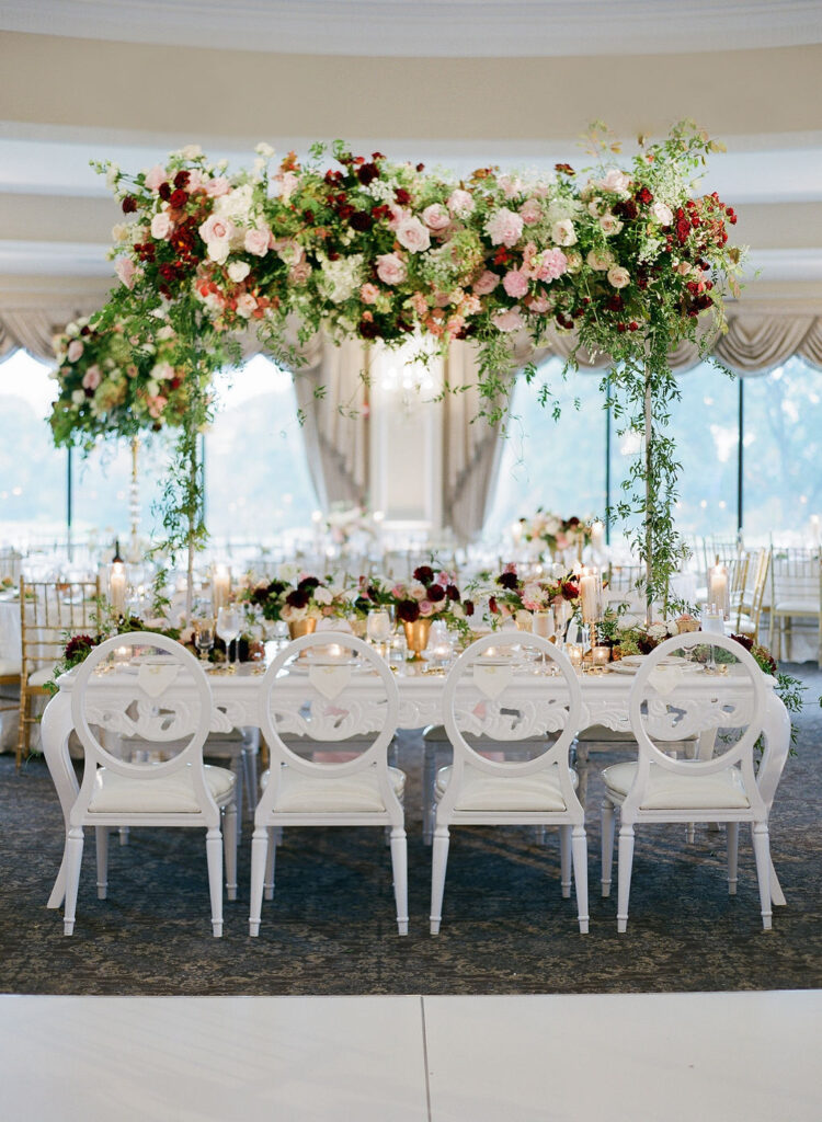 wedding head table with elevated tall centerpiece and white acrylic chairs 