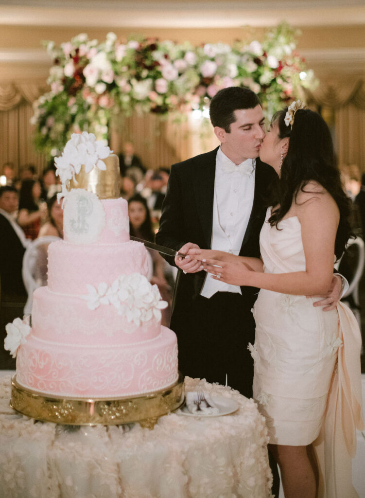 bride and groom cutting pink wedding cake and kissing 