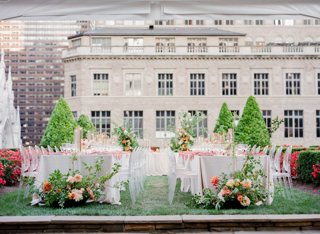 wedding reception with florals on ground and long tables, ghost chairs, and neutral linens 